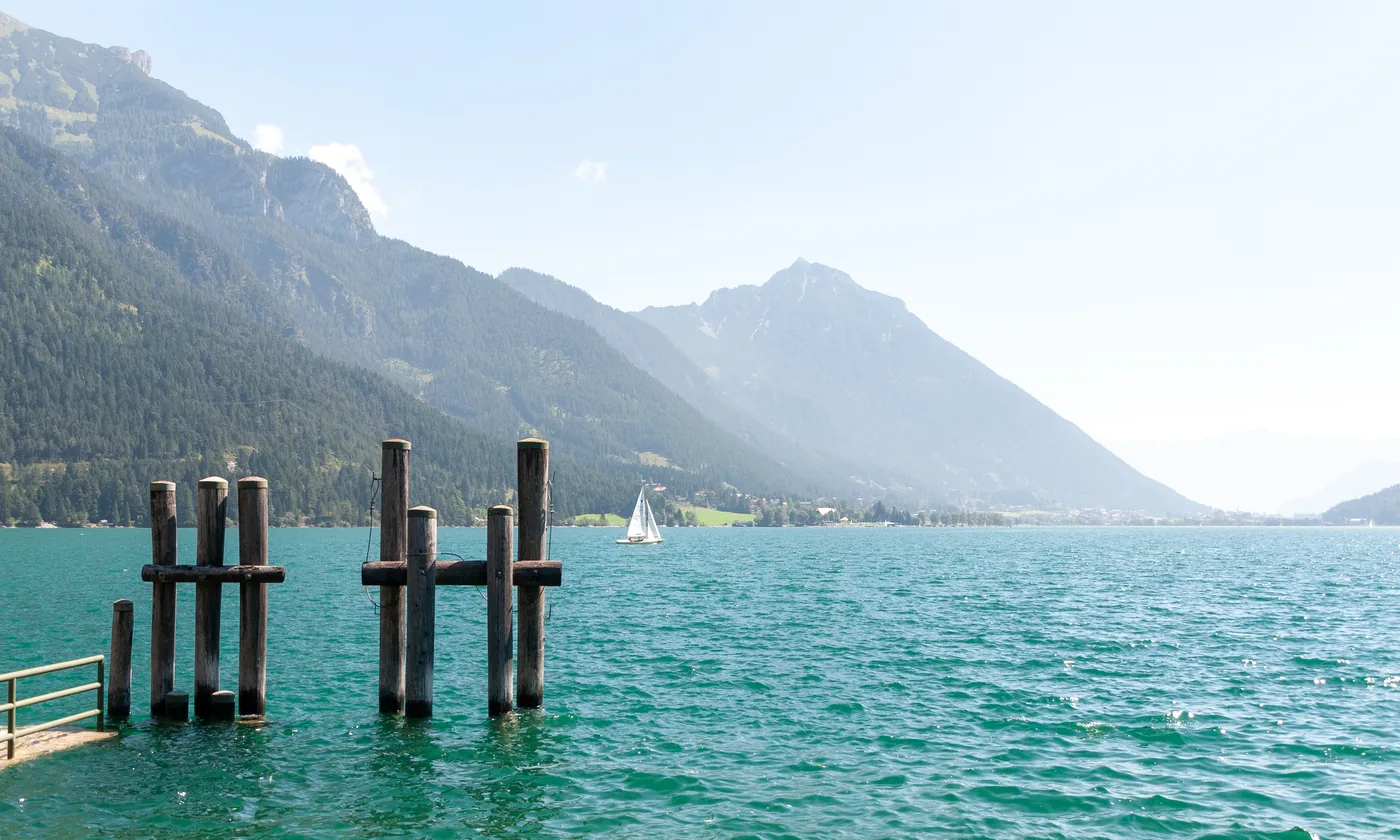 Turquoise water of the Achensee in Tyrol with wooden mooring posts and forested mountains