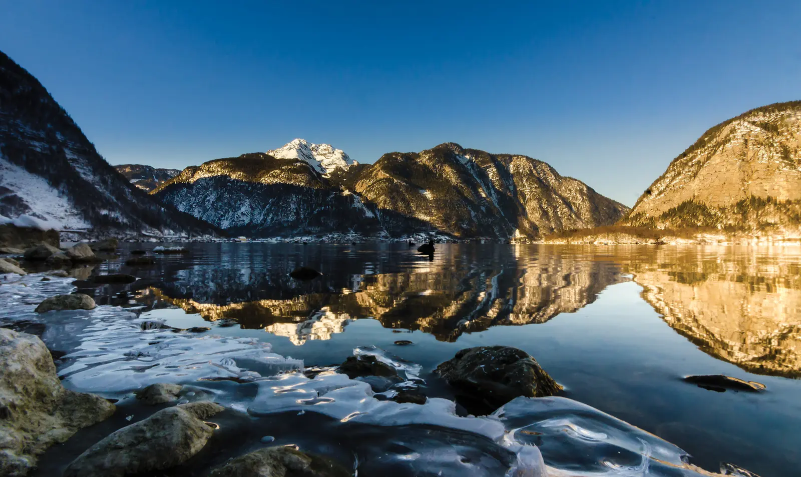 Snowy peaks of the Dachstein range reflected in the still water of Lake Hallstatt on a clear winter morning